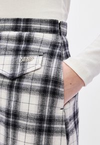 Μαύρη και λευκή καρό φούστα με φερμουάρ, διαθέτοντας ορατή τσέπη και ασημένιο λογότυπο "Tommy Jeans" στο πίσω μέρος.