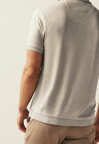 Polo gris à manches courtes avec une texture subtile, doté d'un col en maille plate et d'un ourlet droit, rentré dans un pantalon de couleur claire.