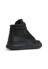 Zapatillas negras de caña alta con un exterior de cuero texturizado y un collar acolchado. Cuentan con una suela gruesa negra y cordones negros para el cierre.