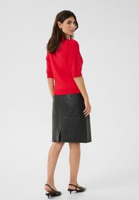 Punainen neulepaita, jossa on lyhyet puffihihat, yhdistetty mustan nahkainen kynähameeseen, jossa on takaläpä ja sileä pinta. Mustat slingback-korkokengät.