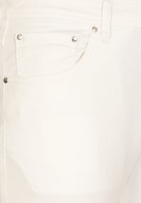 I jeans in denim bianco presentano una tasca frontale visibile con borchie argentate, un design a gamba dritta e linee di cucitura sottili su una trama di tessuto liscia.