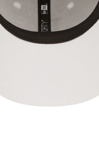 Gorra blanca con visera negra, que cuenta con un forro interior de malla, forma plana y pequeños agujeros de ventilación. Incluye letras negras en el interior.