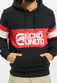 Sudadera con capucha negra que presenta una audaz franja horizontal roja y blanca, un gran logotipo "ECKÓ UNLTD" y un diseño de bolsillo canguro.