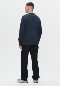 Navy sweatshirt with a crew neckline, textured fabric, ribbed cuffs, and hem, paired with black trousers and grey sneakers.