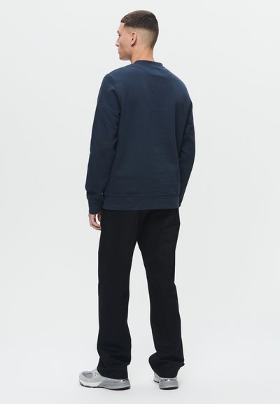 Sweatshirt bleu marine avec un col ras du cou, tissu texturé, poignets et ourlet côtes, associé à un pantalon noir et des baskets grises.