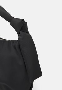 Borsa in tessuto nero con dettaglio nodo sulla tracolla. Presenta una trama liscia e una chiusura con zip lungo il bordo superiore.