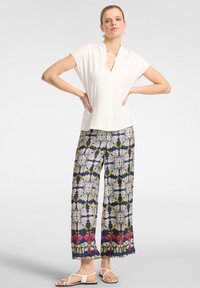 Top bianco a maniche corte abbinato a pantaloni larghi navy a fantasia con disegni floreali in crema, verde e rosa. La modella indossa sandali bianchi.