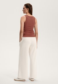 Ribbed brown tank top paired with white wide-leg pants and sneakers, showcasing a fitted silhouette and casual design.