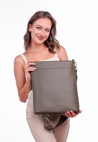 Šedá kožená kabelka s hladkým povrchem, obdélníkovým tvarem, nastavitelným popruhem a jemně vyraženým logem ve spodní části.