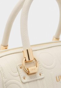 Borsa a tracolla in pelle bianca strutturata con hardware dorato, dotata di manici arrotondati e un'etichetta decorativa. Sottile motivo circolare stampato a rilievo.
