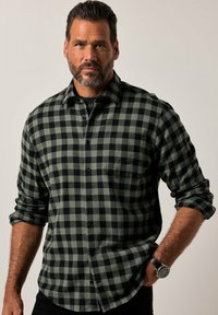 Camicia in flanella a quadri verde scuro e nero, con maniche lunghe, chiusura con bottoni e taschino sul petto. Tessuto morbido, vestibilità comoda.