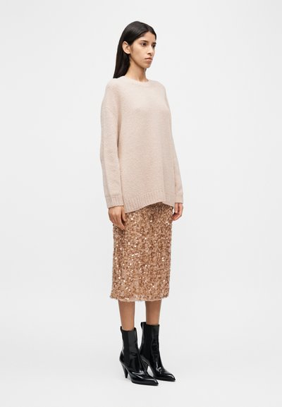 Ροζ ανοιχτόχρωμο πλεκτό πουλόβερ σε μεγάλο μέγεθος με υφή, συνδυασμένο με φούστα μέχρι το γόνατο με παγιέτες σε ροζ χρυσό και μαύρα μυτερά μποτάκια αστραγάλου.