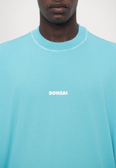 Turquoise short-sleeve t-shirt made of soft cotton, featuring a white logo "BONSAI" centered on the chest. Minimalist design with a round neckline.