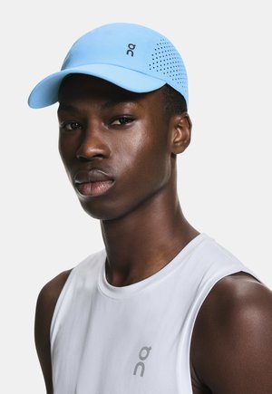 Young man wearing a light blue perforated sports cap and a sleeveless white athletic shirt with gray logo on chest.