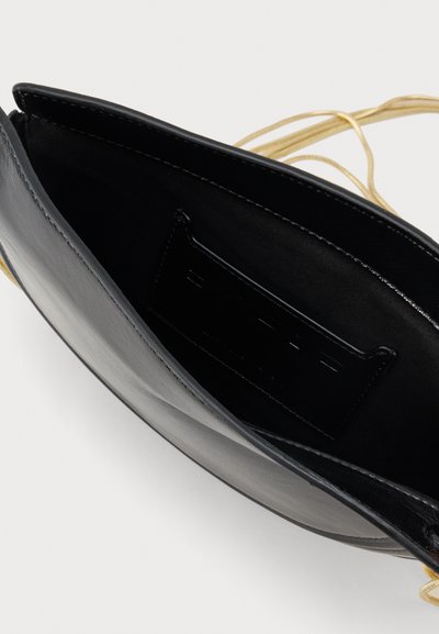 Bolsa de couro preto com uma textura suave, apresentando um compartimento interior e um fecho de cordão em tom dourado. Rótulo da marca visível no interior.