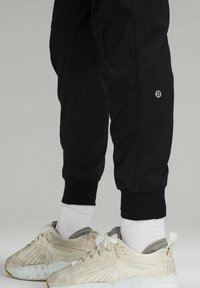 Schwarze sportliche Jogginghosen mit gerippter Textur, elastischem Bund und Bündchen. Kombiniert mit weißen Crew-Socken und cremefarbenen Turnschuhen.