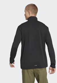 Black long-sleeve top with a high collar, made of lightweight material. Features a straight hem and a small logo near the bottom.