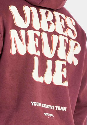 Bordeauxfarbener Hoodie mit auffälliger, retro inspirierter, weißer Schrift: "VIBES NEVER LIE" und "YOUNG CREATIVE TEAM" nahe dem Saum. Weicher Stoff.