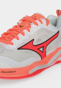 Λευκό και κοραλλί αθλητικό παπούτσι Mizuno με κορδόνια σε κοραλλί χρώμα και κόκκινο λογότυπο Mizuno στο πλάι, με αντικραδασμική τεχνολογία Mizuno Energy XP.