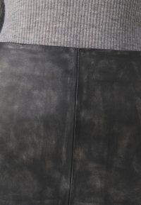 Črna usnjena materiala z gladko teksturo, v kombinaciji z žametenim sivim materialom na vrhu, ki prikazuje prilegajočo se zasnovo in čiste šive.