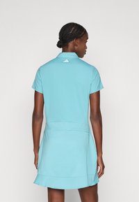 Svetlo modra kratkotrajna polo obleka z razširjenim spodnjim delom in ovratnikom. Ima logo Adidas na hrbtu in gladek, raztegljiv material.