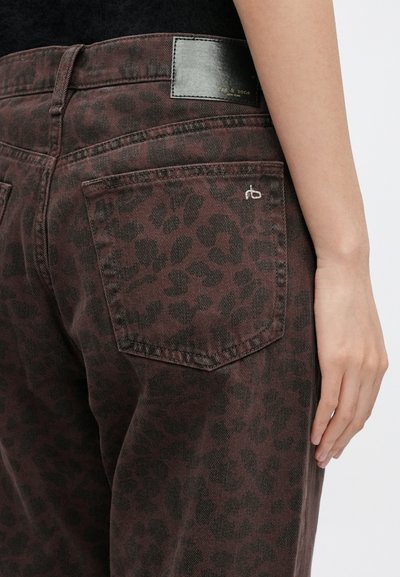 Hnedé rifle z denimu so subtílnym leopardím vzorom, s čiernou koženou nášivkou v páse a vyšívaným logom na zadnom vrecku.