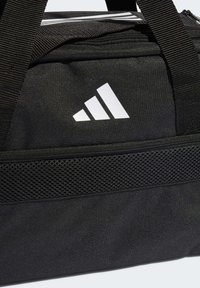 Mustkast, millel on tekstureeritud nailonist välimus, mesh-tasku, valge logo ja tugevad mustad vöörihmad. Lukuga peamine sektsioon.