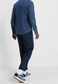 Tummansininen farkkupaita pitkillä hihoilla, yhdistettynä tummansinisiin kapeneviin housuihin. Jalkineet koostuvat valkoisista sukista ja sinisistä lenkkareista mustilla yksityiskohdilla.