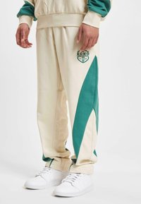 Beige joggebukser med grønne sidepaneler, som har et Ecko Unlimited-logo. Laget av myk bomullsblanding, designet for komfort og uformell bruk.