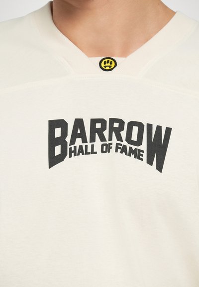 Cream-colored T-shirt with a rounded neckline featuring a black graphic reading "BARROW HALL OF FAME" and a small yellow smiley accent.