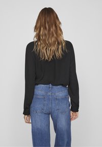 Blouse noire à manches longues associée à un jean en denim bleu taille haute, doté de poches latérales et d'une coupe décontractée.