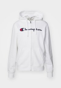 Hvit zip-up hettejakke laget av mykt stoff, med en fremre lomme og en stor brodert "Champion" logo i marineblått og rødt.