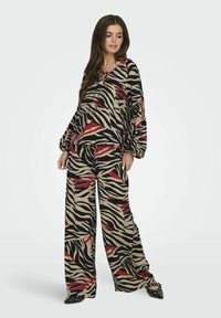 Set da salotto con stampa zebra, composto da un top ampio con maniche a sbuffo e pantaloni a gamba larga nei colori beige, nero e rosso. Texture di tessuto morbido.