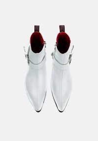 White ankle boots with pointed toes, smooth leather texture, silver hardware, and contrasting red interior. Side zippers and strap detail included.