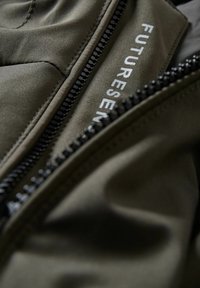 Olivově zelená bunda s hladkým povrchem, vybavená černým zipem a nápisem "FUTURE-SENSE" v bílé barvě na látce.