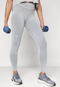Leggings grises de tiro alto con textura acanalada, que presentan costuras en los paneles laterales. Junto con zapatillas deportivas grises y un dumbbell azul.