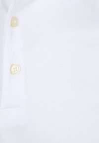 Witte poloshirt van een textuurstof. Voorzien van een knopenlijst met een enkele beige knop en versterkte stiksels rond de kraag.