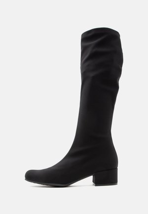 Schwarzer Stiefel bis zur Mitte der Wade mit niedrigem Blockabsatz und abgerundeter Spitze, schlaffer Stoffschaft, seitlich vor weißem Hintergrund gezeigt.