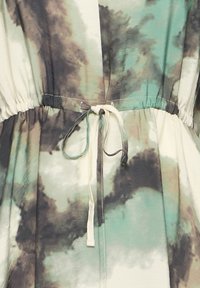 Pás oblečenia s batikovaným vzorom v zelených, čiernych a béžových farbách, s látkovou šnúrkou zviazanou do mašle.