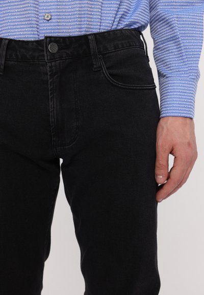 Schwarze Denim-Jeans mit schmaler Passform, ausgestattet mit Fronttaschen und Knopfverschluss. Kombiniert mit einem blauen gemusterten Langarmhemd.