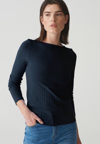 Marineblaues Langarmoberteil mit gerippter Textur, Rundhalsausschnitt und schlanker Passform. Kombiniert mit hellblauer Denim, die über eine Fronttasche verfügt.