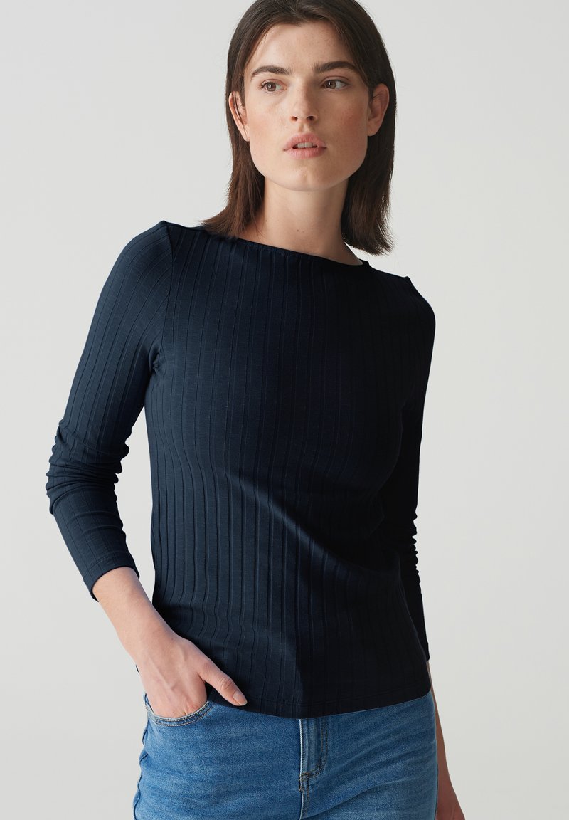 Marineblaues Langarmoberteil mit gerippter Textur, Rundhalsausschnitt und schlanker Passform. Kombiniert mit hellblauer Denim, die über eine Fronttasche verfügt.