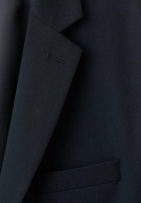 Marineblauw getailleerd colbert met een gestructureerde stof, een reverskraag met inkeping en een enkele zakdetail. Subtiele merkopdruk op de mouw.