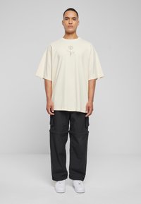 Beige oversized t-skjorte med en roseillustrasjon i midten, parret med svarte cargo-bukser og hvite sneakers. Glatt stoff, avslappet passform.