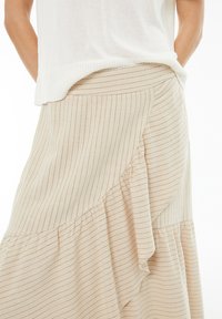 Falda de rayas beige con un diseño acampanado, que presenta un dobladillo con volantes y una textura suave. Corte a la cintura y tejido ligero y transpirable.