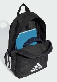 Mochila negra hecha de un tejido duradero, con un diseño de tres rayas blancas, un compartimento principal con cremallera y un bolsillo delantero con tapa.