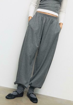 Wide gray pinstriped pants with elastic waistband, worn with gray scrunched socks and black Mary Jane flats, paired with a cropped long-sleeve top.