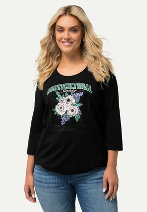 Zwarte langharige shirt met een bloemenafbeelding in wit en paars met tekst, gecombineerd met lichtblauwe denim jeans.