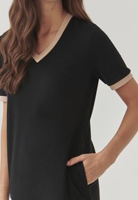 Czarna sukienka o krótkich rękawach z dekoltem w serek, z beżowym wykończeniem wzdłuż kołnierza i rękawów, oraz z bocznymi kieszeniami dla funkcjonalności.