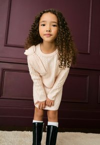 Gaiši rozā adīta svārku kleita ar kabelīša adījumu, pērļu akcentiem un plecu loku. Melni spīdīgi ceļgalu augstie zābaki ar baltu apdari.